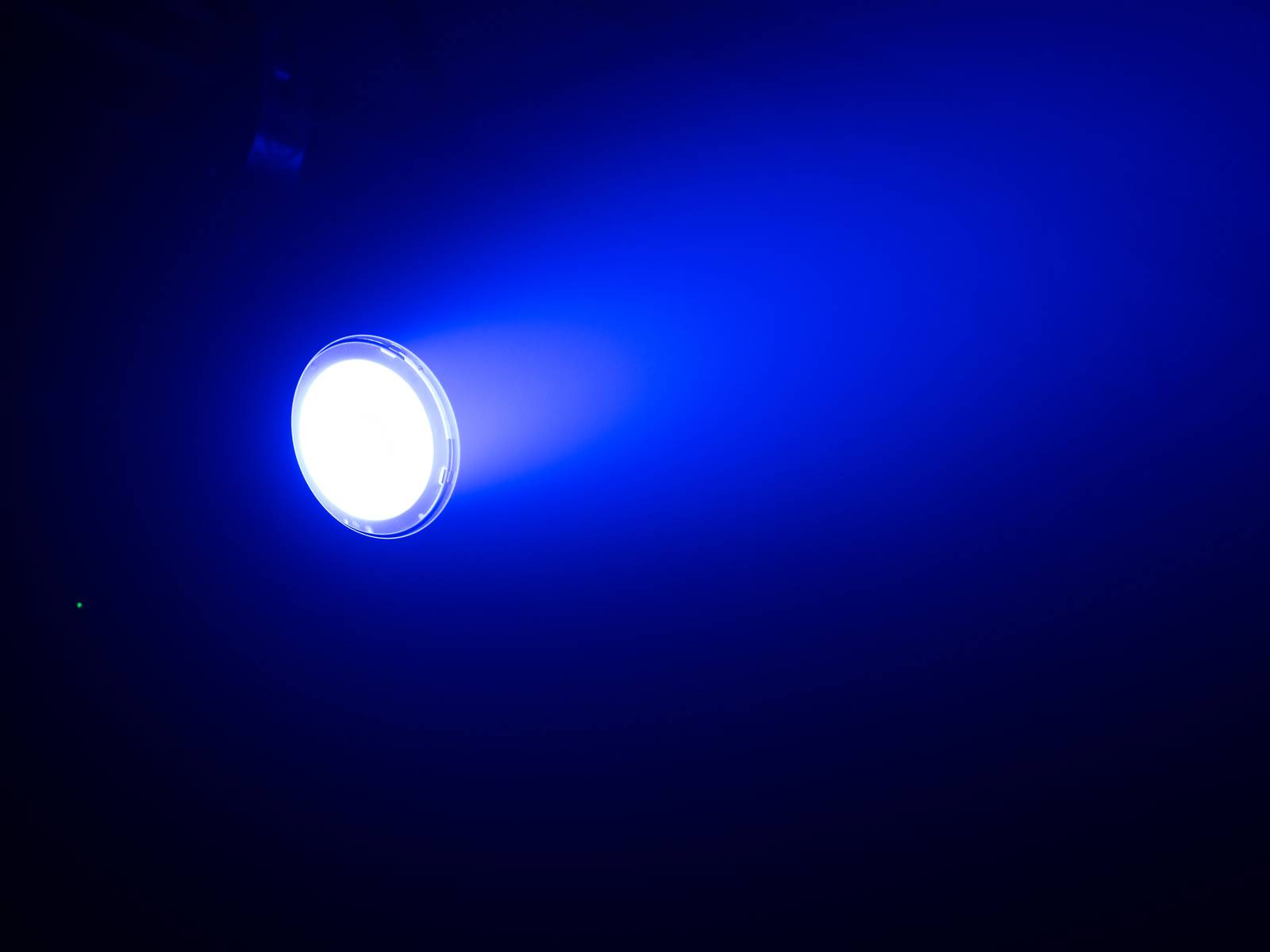 Jasný, kulatý reflektor vyzařuje modré světlo do tmavé místnosti.