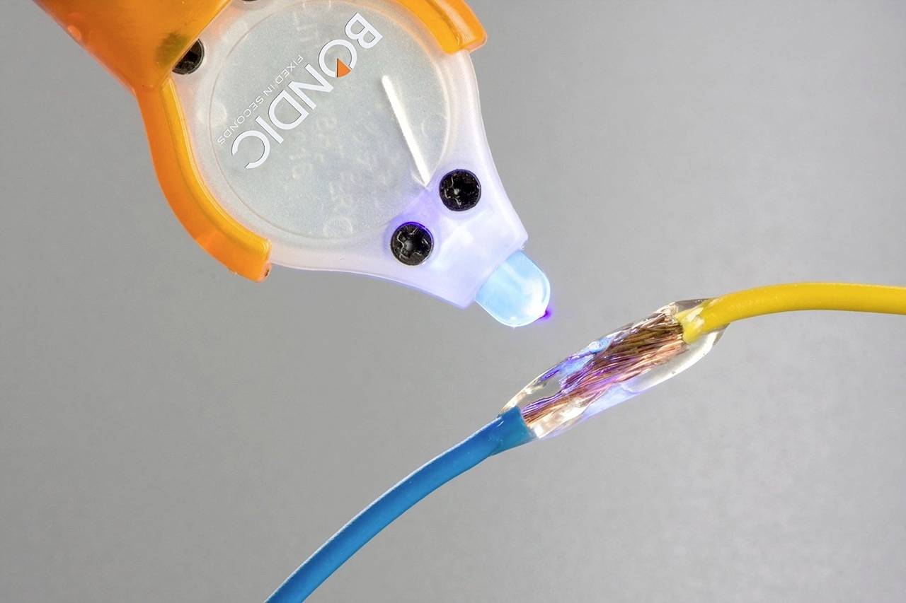 Detailní pohled na lepený spoj dvou drátů s UV lepidlem, přičemž jeden kabel je oranžový a druhý modrý.