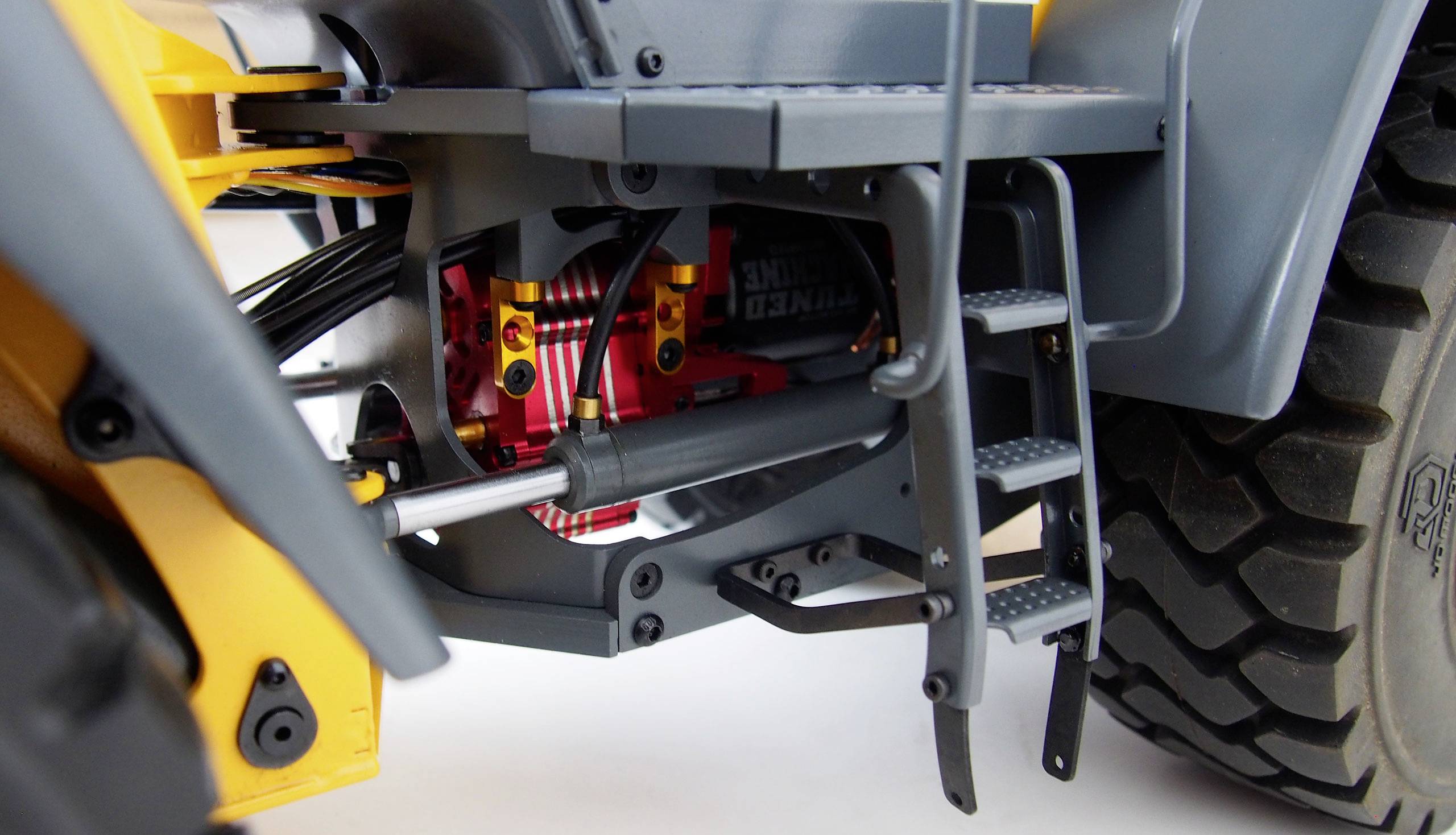 Detailní záběr stavebního vozidla, zobrazující žebřík a technické komponenty, jako jsou hydraulické hadice a dezén pneumatiky.