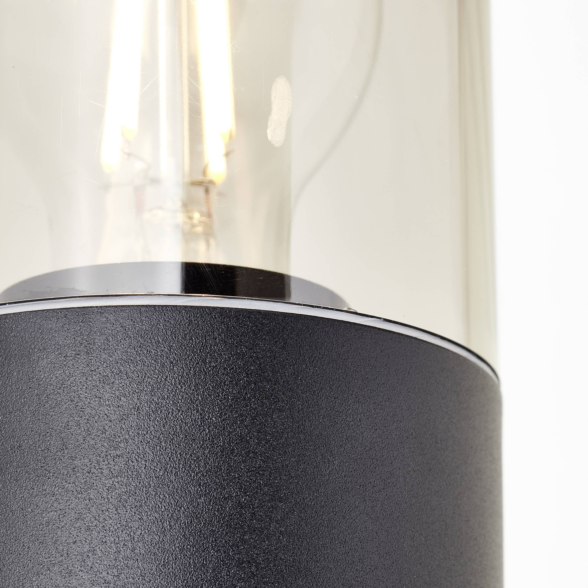 Detailní záběr moderní lampy s průhledným sklem a viditelným žhnoucím vláknem. Základna je vyrobena z černého kovu.