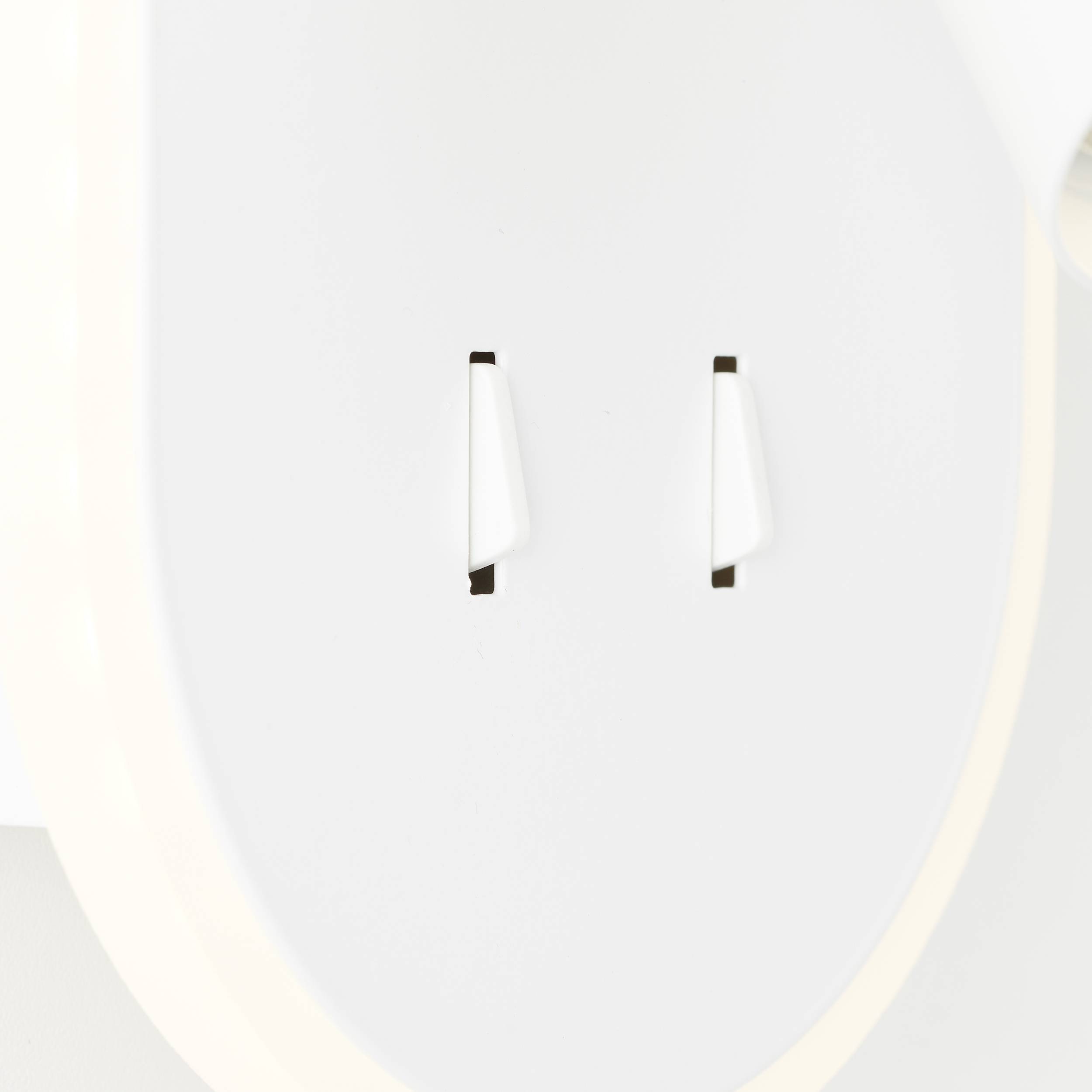 Detailní záběr bílé elektrické zásuvky se dvěma otvory, minimalisticky navržené, na světlém pozadí.
