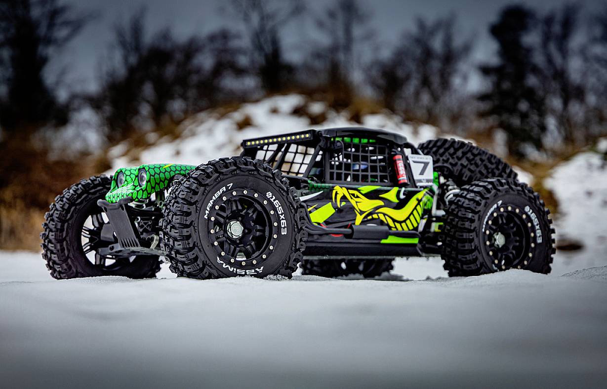Dálkově ovládané auto s agresivním designem a zelenou kresbou na karoserii jede přes zasněženou plochu.