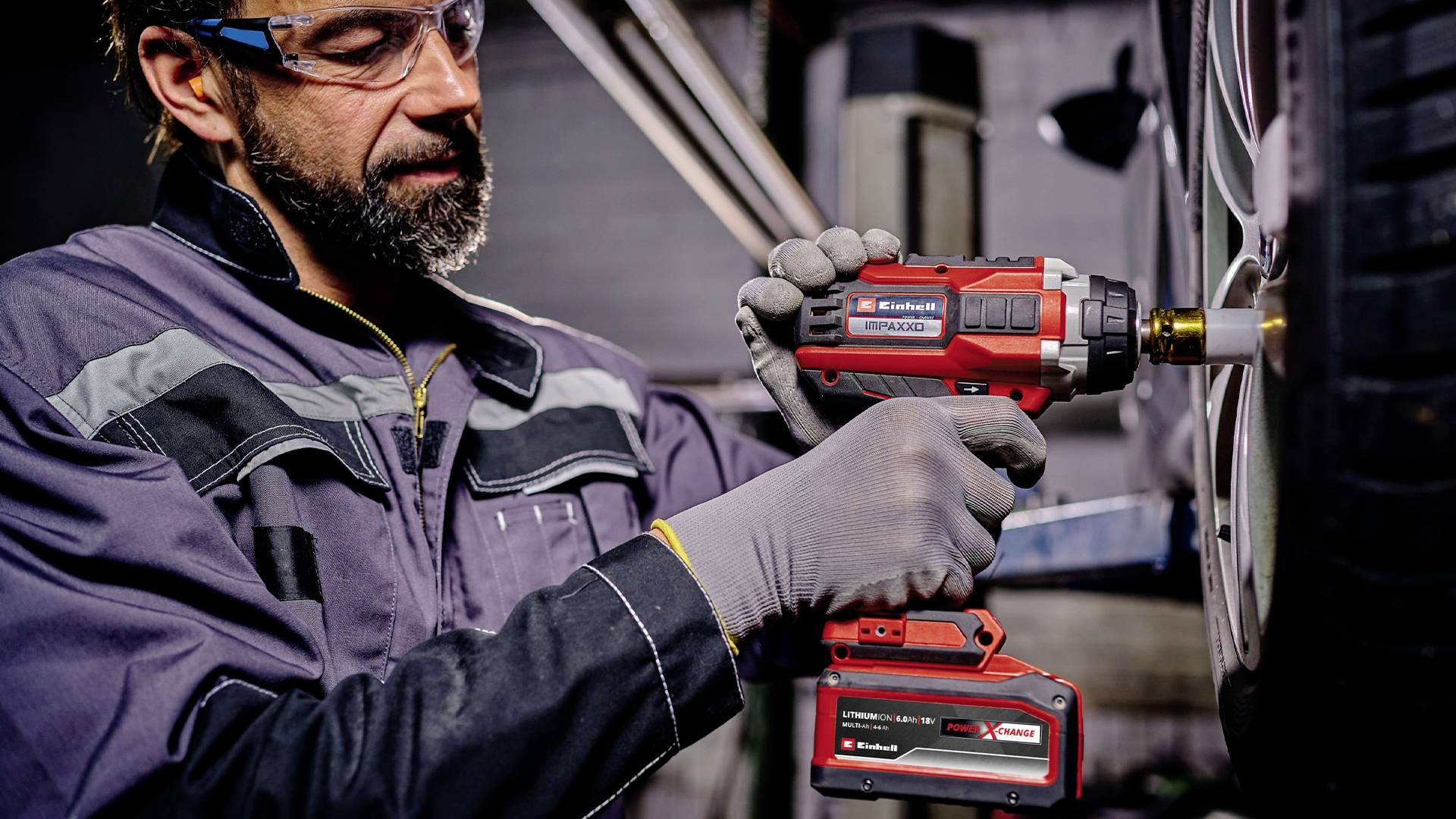 Mechanik utahuje pomocí červeného akumulátorového šroubováku kolové matice na pneumatice automobilu. Má ochranné brýle a pracovní oděv.