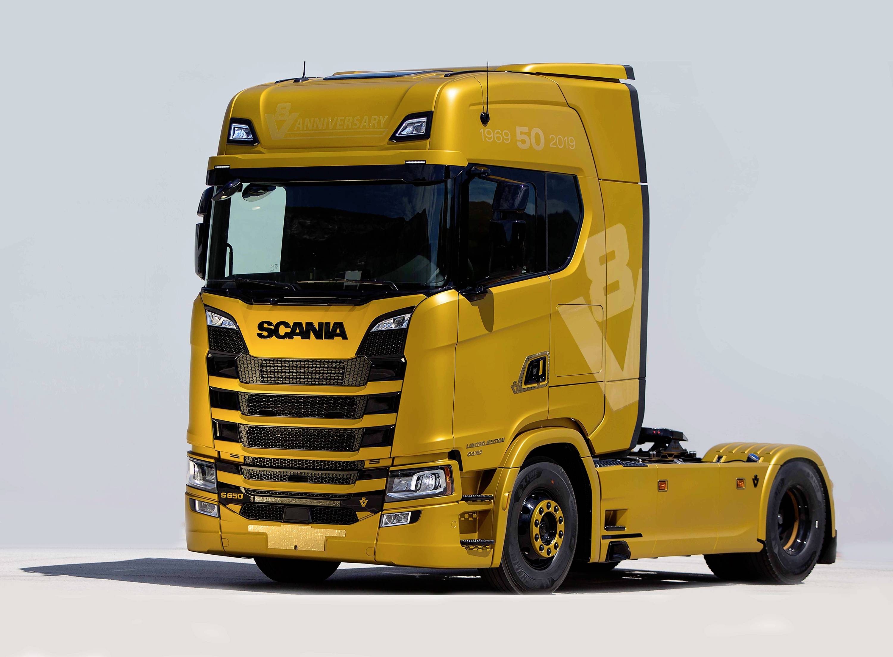 Žlutý nákladní vůz Scania, model R 500, fotografovaný z čelního a bočního pohledu, na světle modrém pozadí.