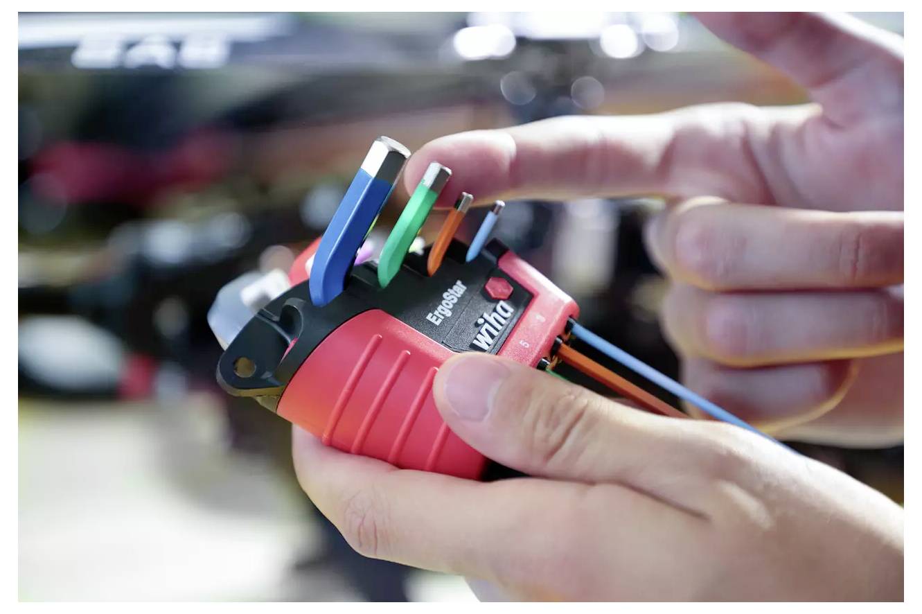 Ruce držící zařízení s barevnými vodiči, ilustrující elektrickou instalaci nebo zapojení.