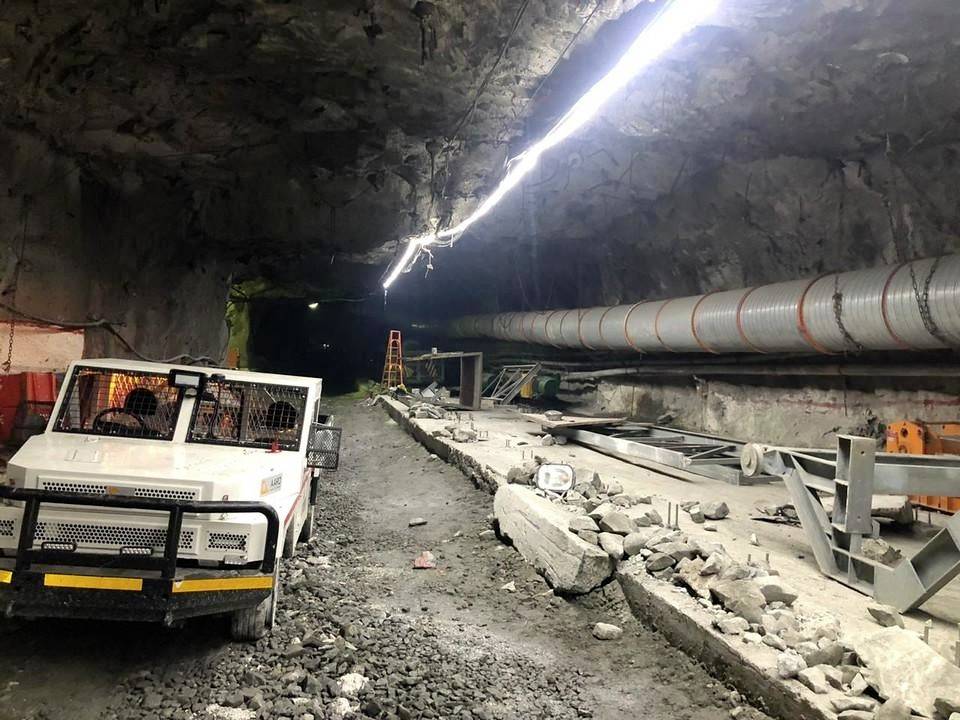 Stavební práce v tunelu s vozidlem a větracím systémem. Stavební materiály a sutě jsou rozházené po podlaze.