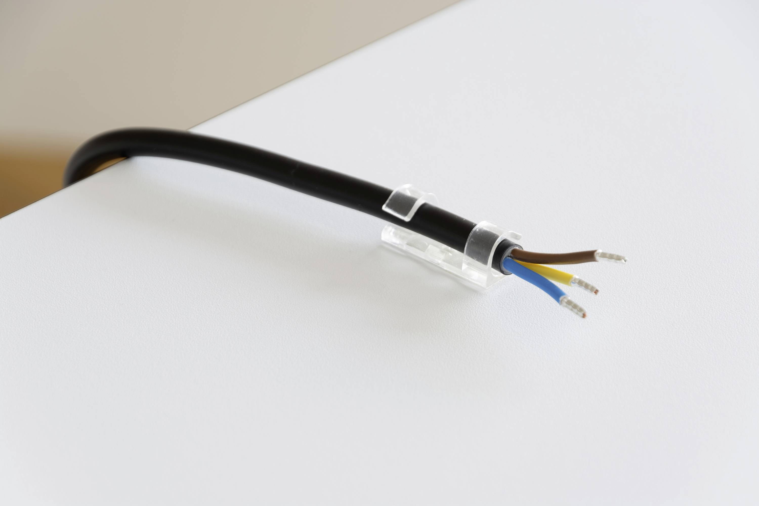 Přerušený elektrický kabel s izolovanými měděnými vodiči v černé, modré a hnědé barvě leží na bílém povrchu.