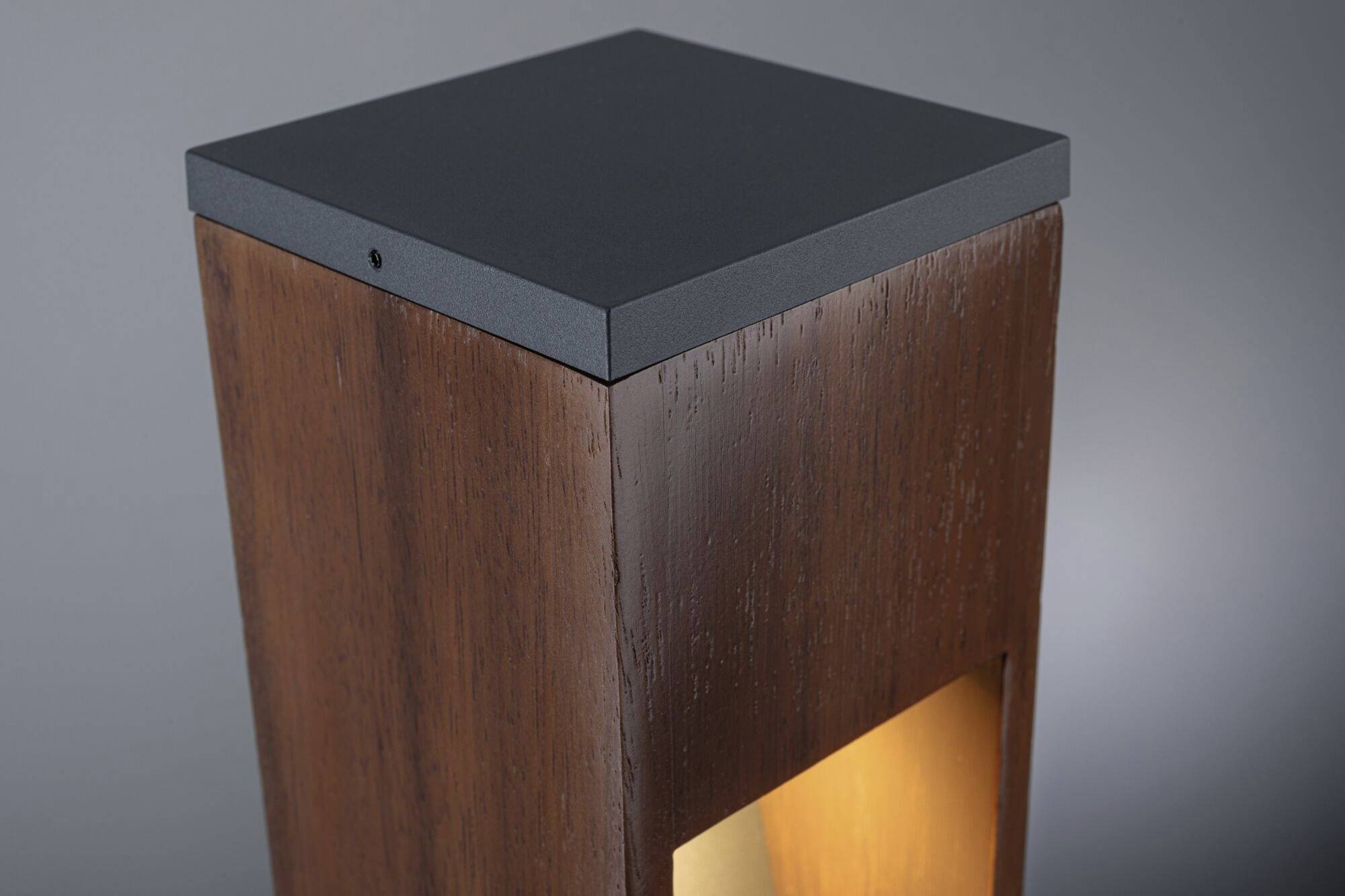 Dřevěný sloup se zabudovaným světlem, které vytváří teplé žluté světlo, před šedým pozadím. Minimalistický a moderní design.