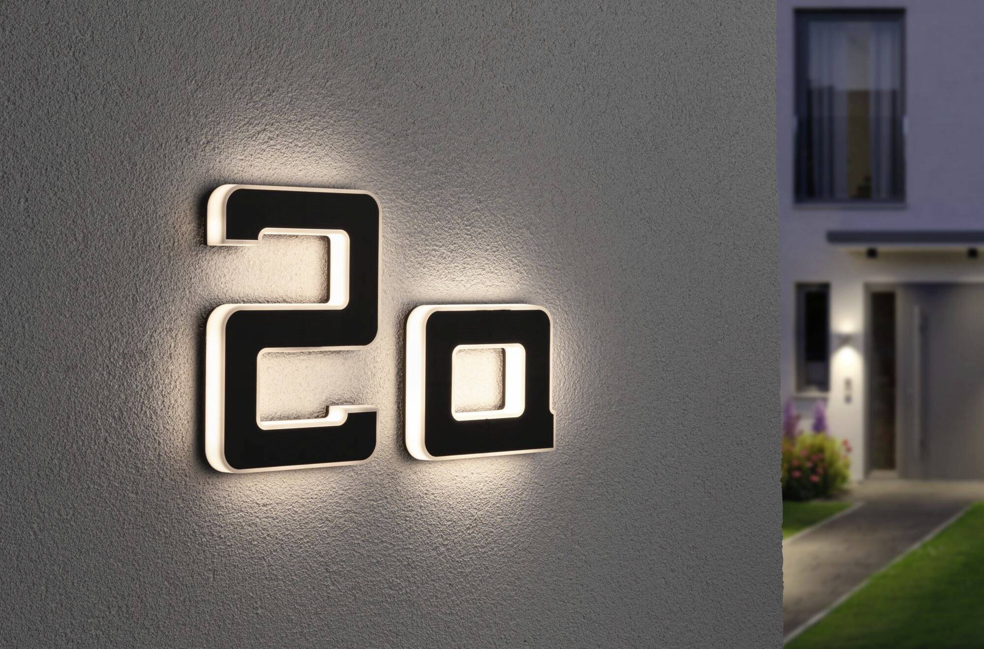 Číslo domu '20', osvětlené na stěně moderního domu se zastřeným pohledem na zahradu a vstupní prostor v pozadí.
