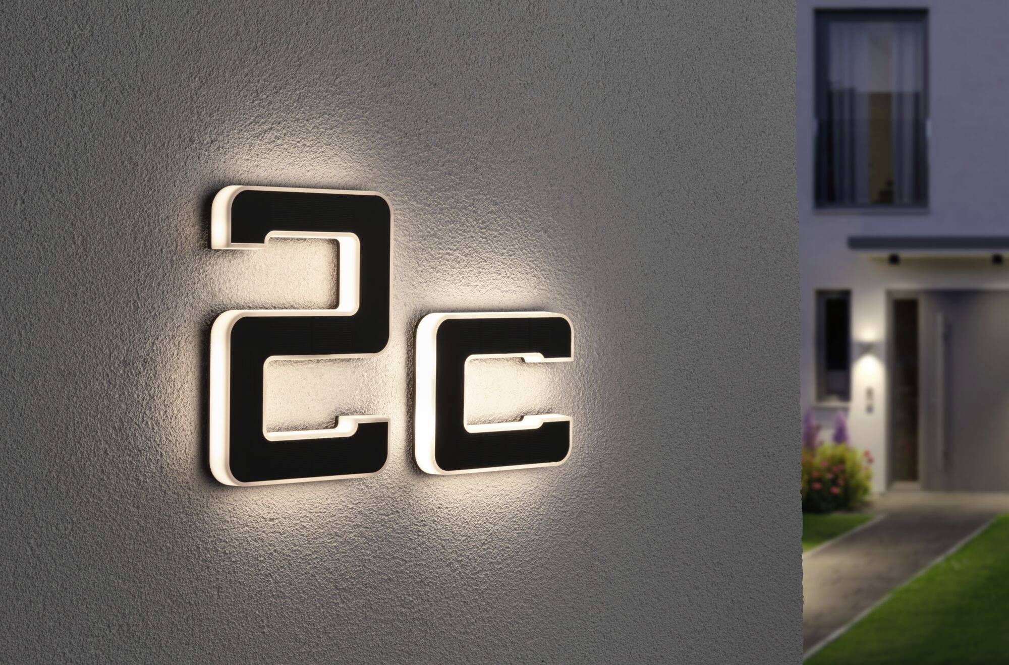 Číslo domu '2c' na osvětlené zdi. V pozadí je vidět část domu se vstupem.