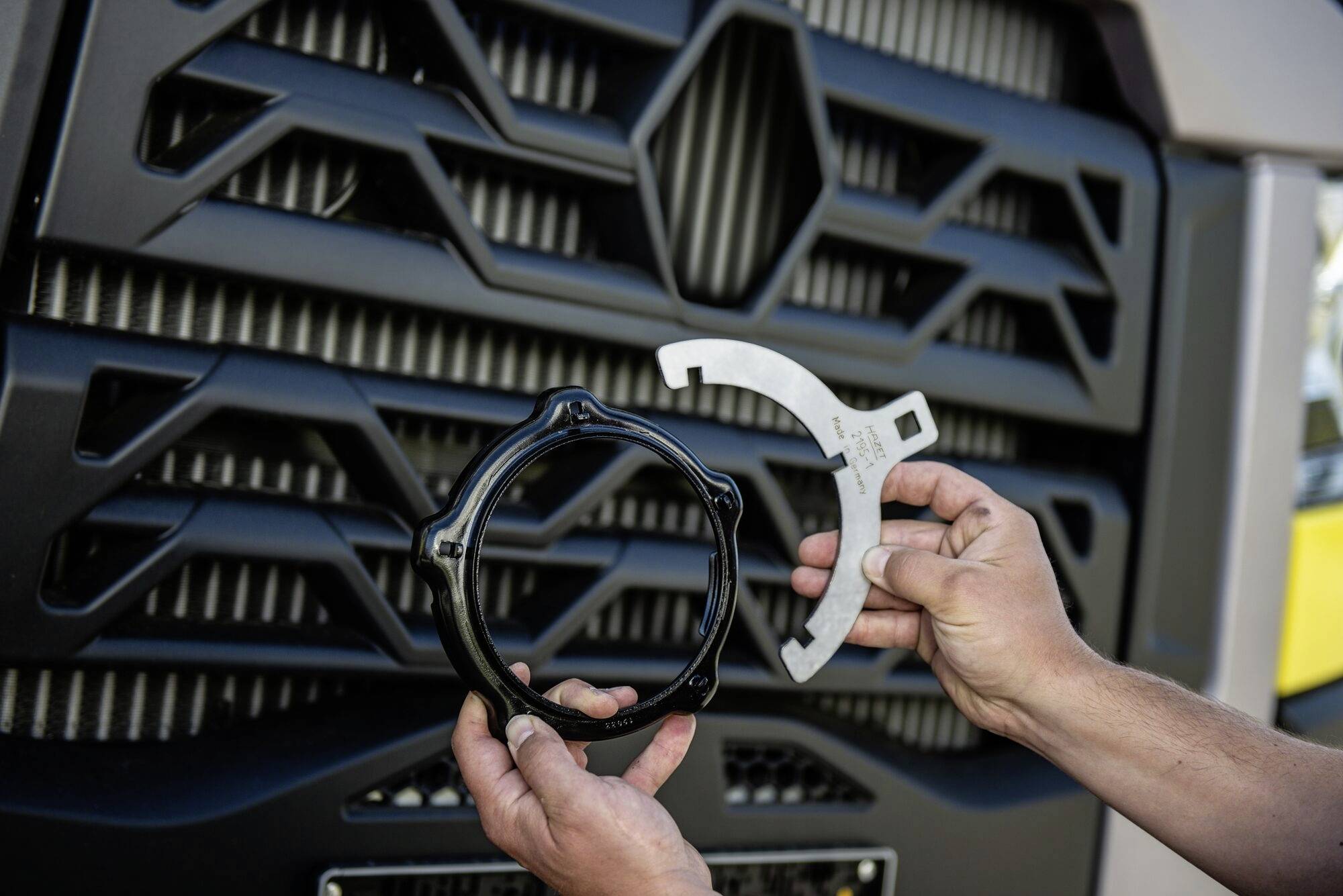 Osoba drží dvě části vozidla před chladičovou mříží nákladního automobilu.
