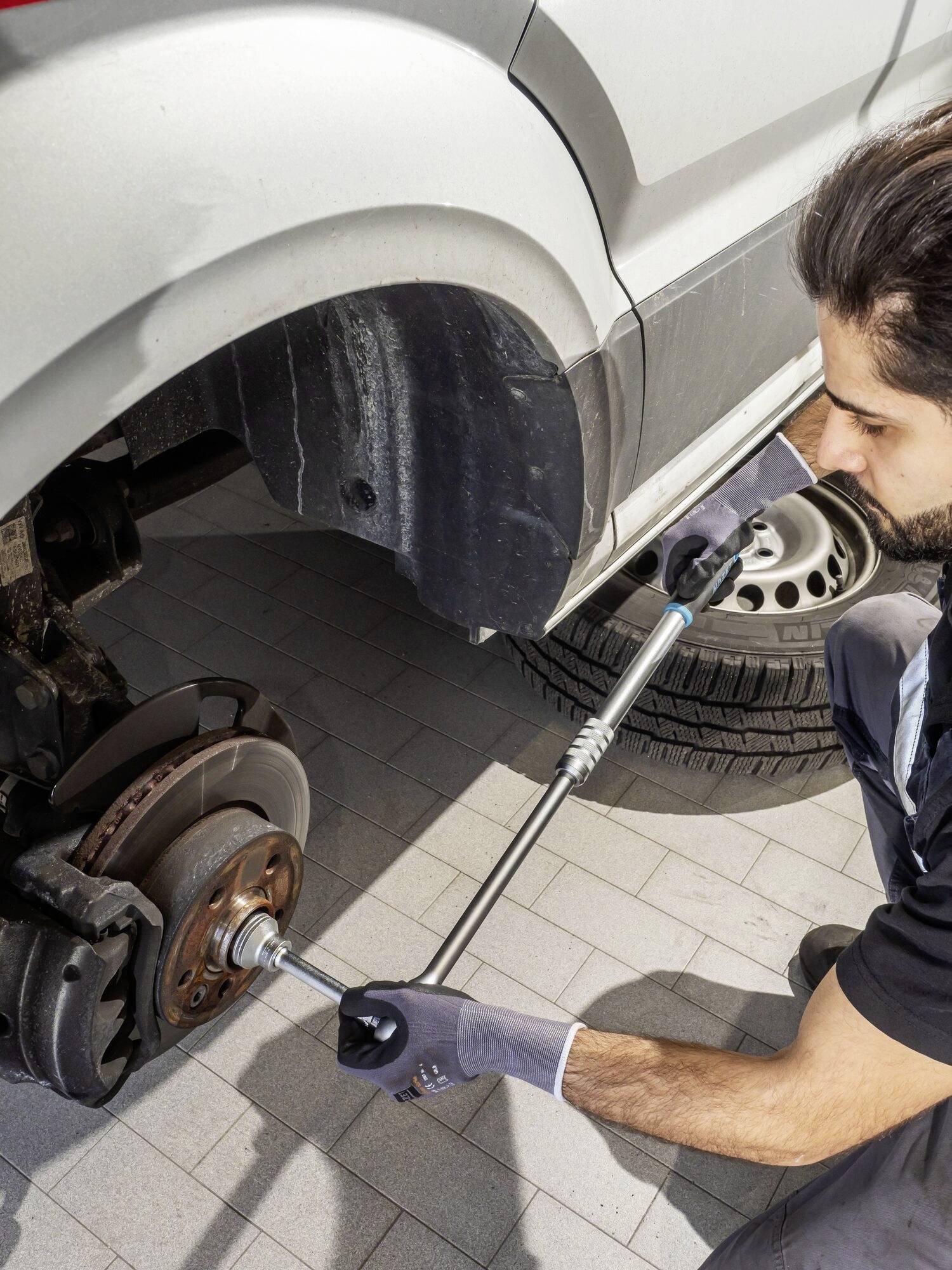 Mechanik vymění brzdový kotouč pomocí rázového utahováku v autoservisu. Auto je zvednuté na zvedáku.