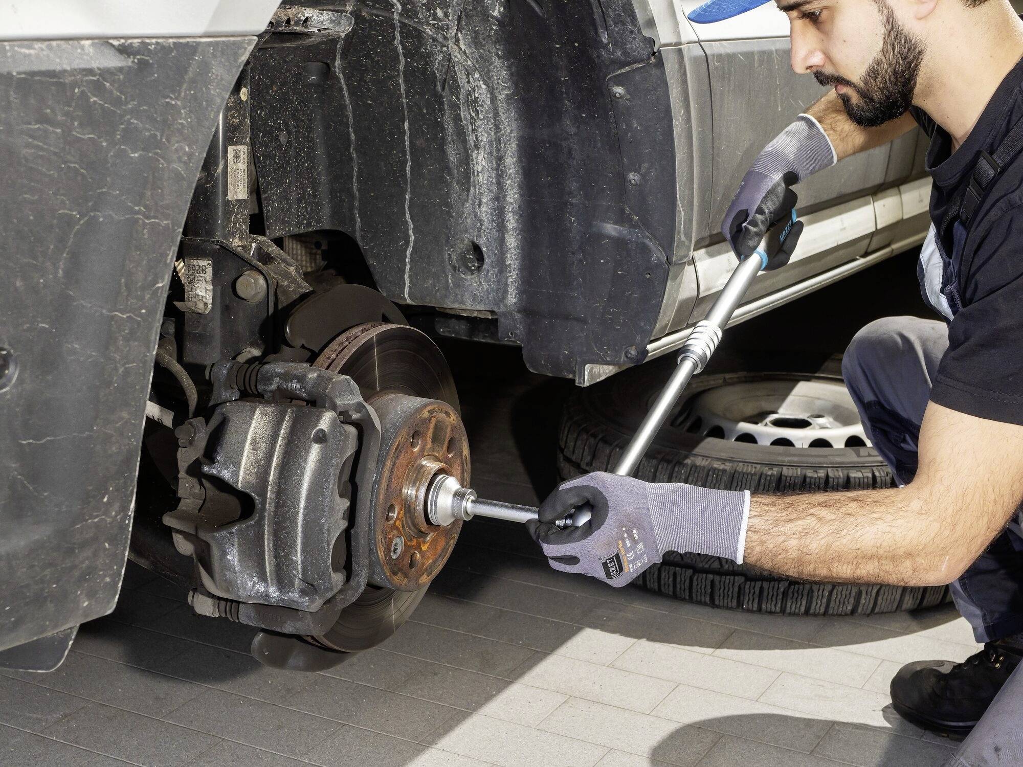 Mechanik vyměňuje kolo automobilu pomocí klíče. Auto je zvednuté a zadní kolo je sundané.