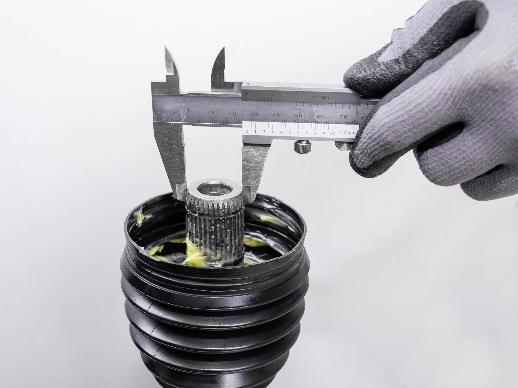 Osoba měří ozubené kolo v hřídelové spojce pomocí posuvného měřítka, které je pokryto tukem.