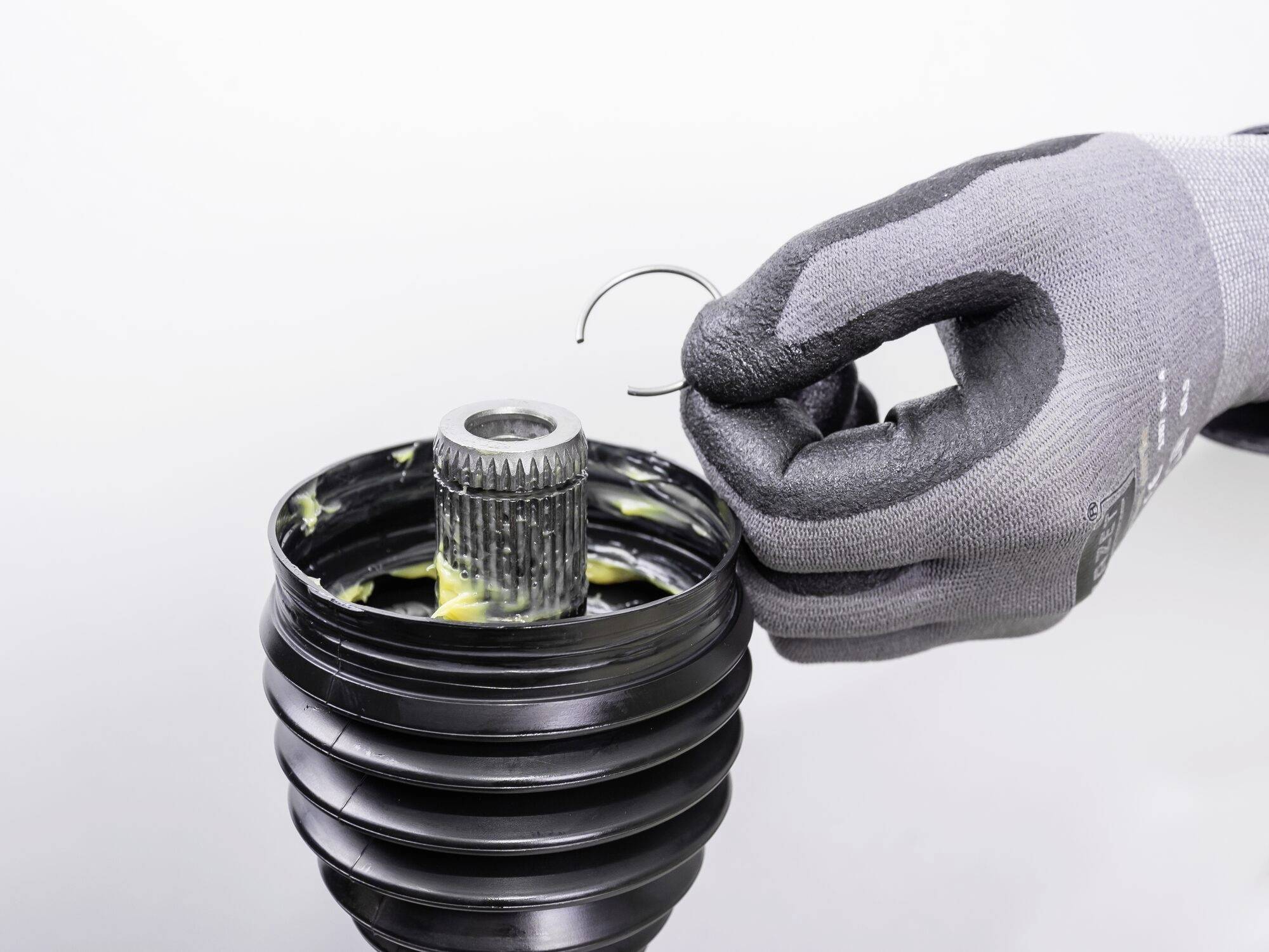 Oděná ruka drží kovový klip nad promazanou mechanickou součástkou.