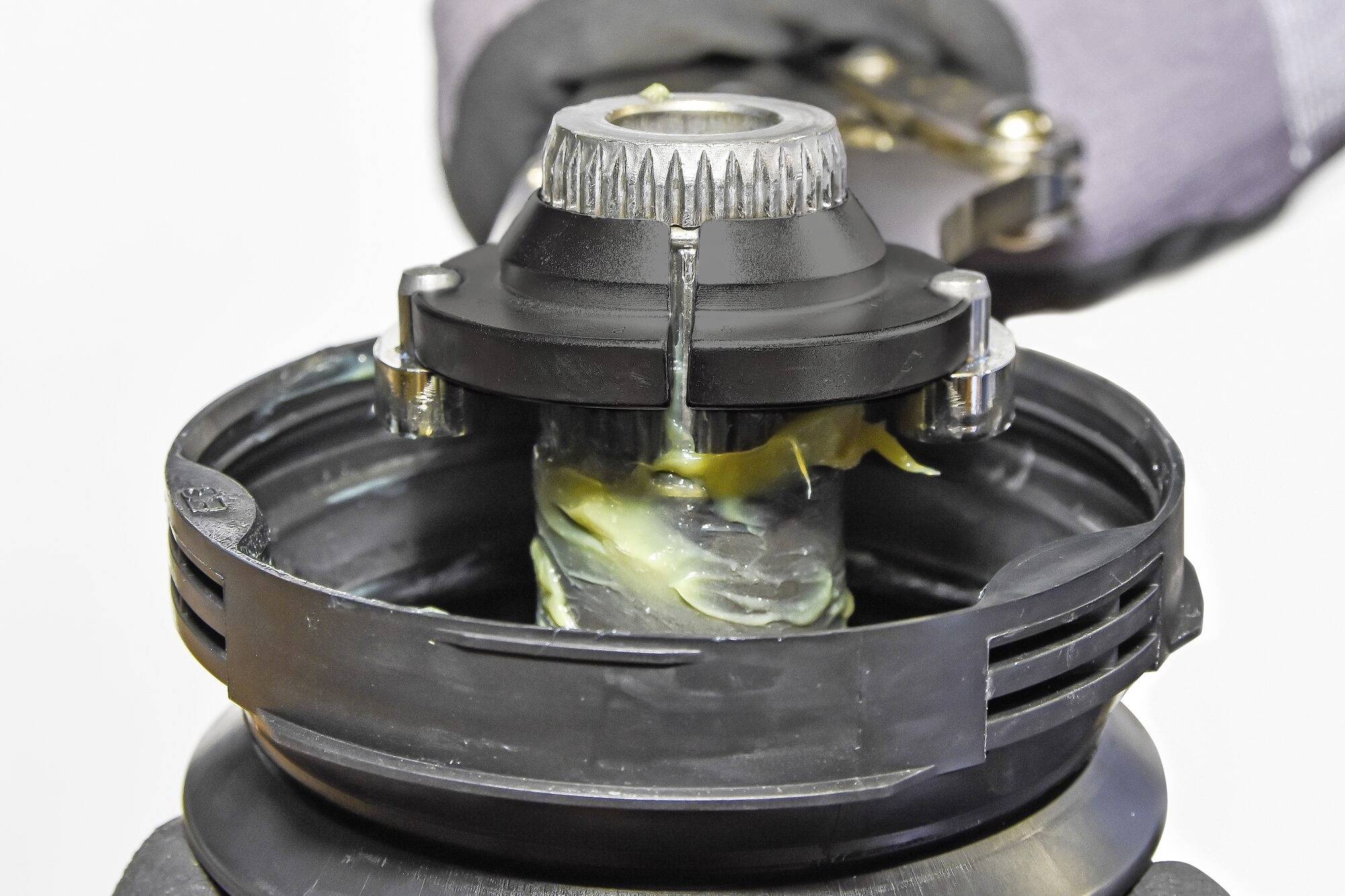 Detailní záběr strojní součástky s mazivem. Osoba drží součástku během údržby nebo opravy.