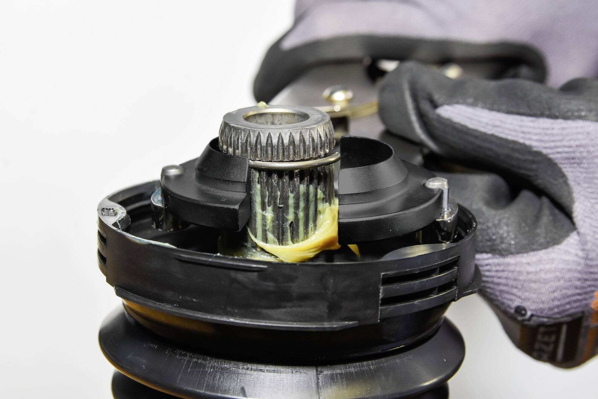 Detailní záběr dělníka v rukavicích, který maže strojní pohonnou součástku mazivem za účelem provedení údržby.