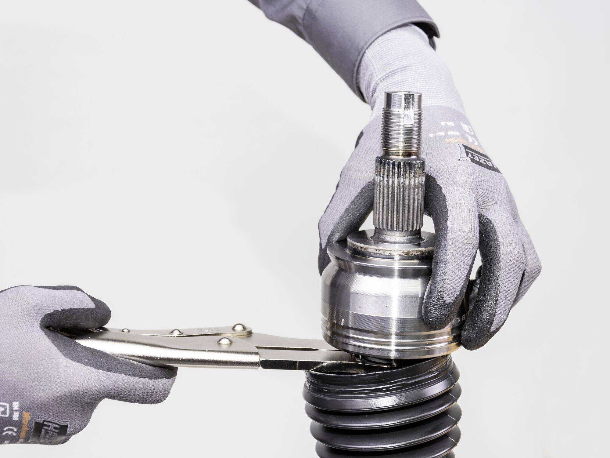 Dvě ruce v šedých rukavicích drží kovový mechanismus, zatímco kleště upevňují mechanismus na černém měchu.