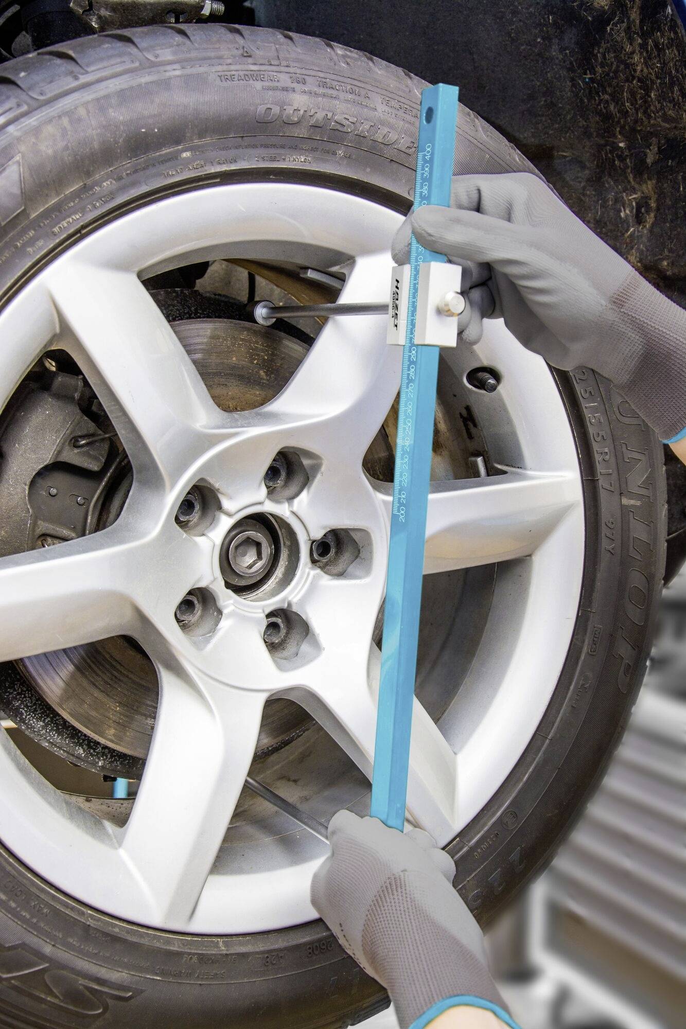 Osoba měří vzdálenost automobilového kola pomocí modrého měřicího přístroje. Pneumatika a ráfek jsou dobře viditelné.