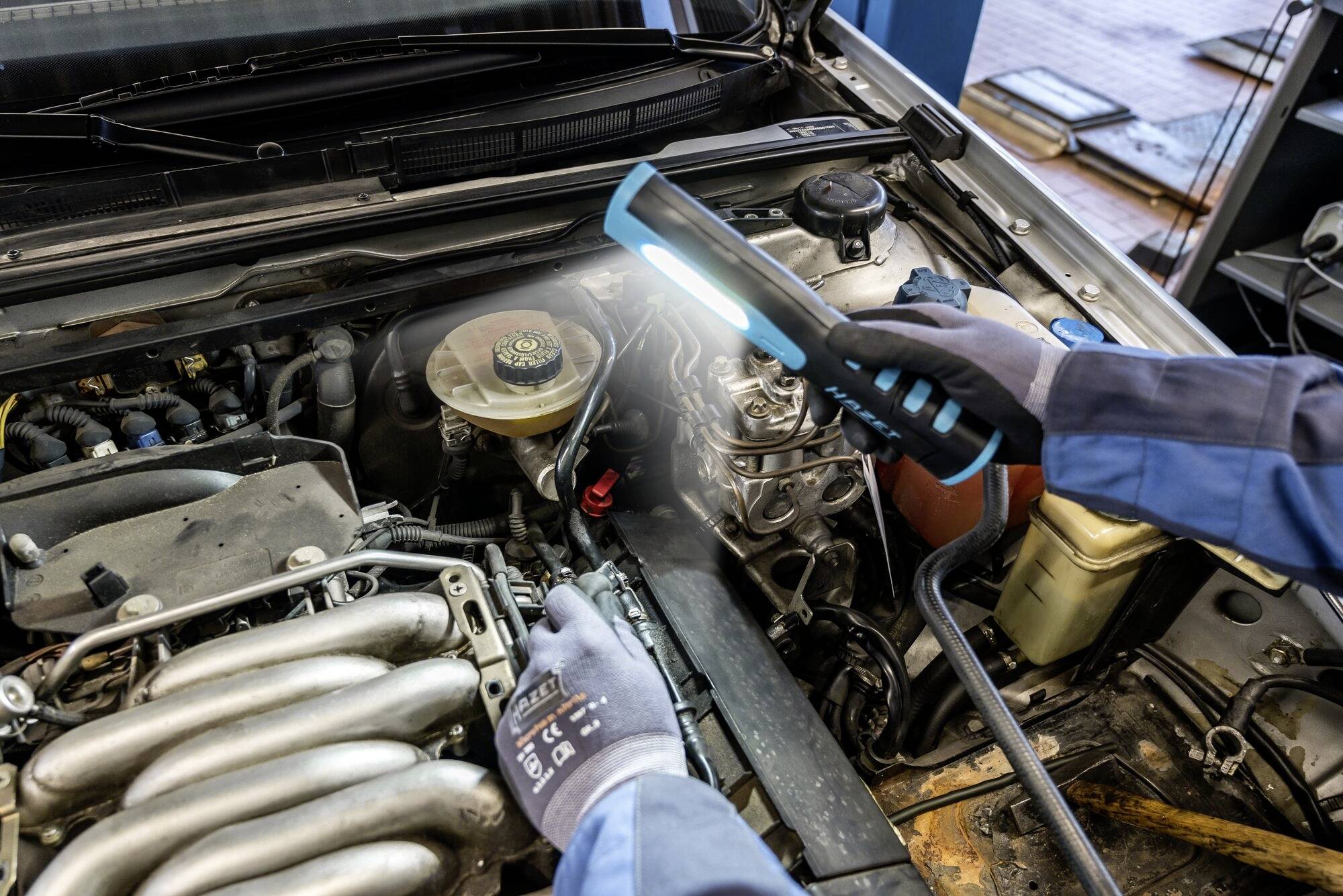 Mechanik kontroluje motorový prostor automobilu pomocí kapesní svítilny, aby provedl údržbářské práce.