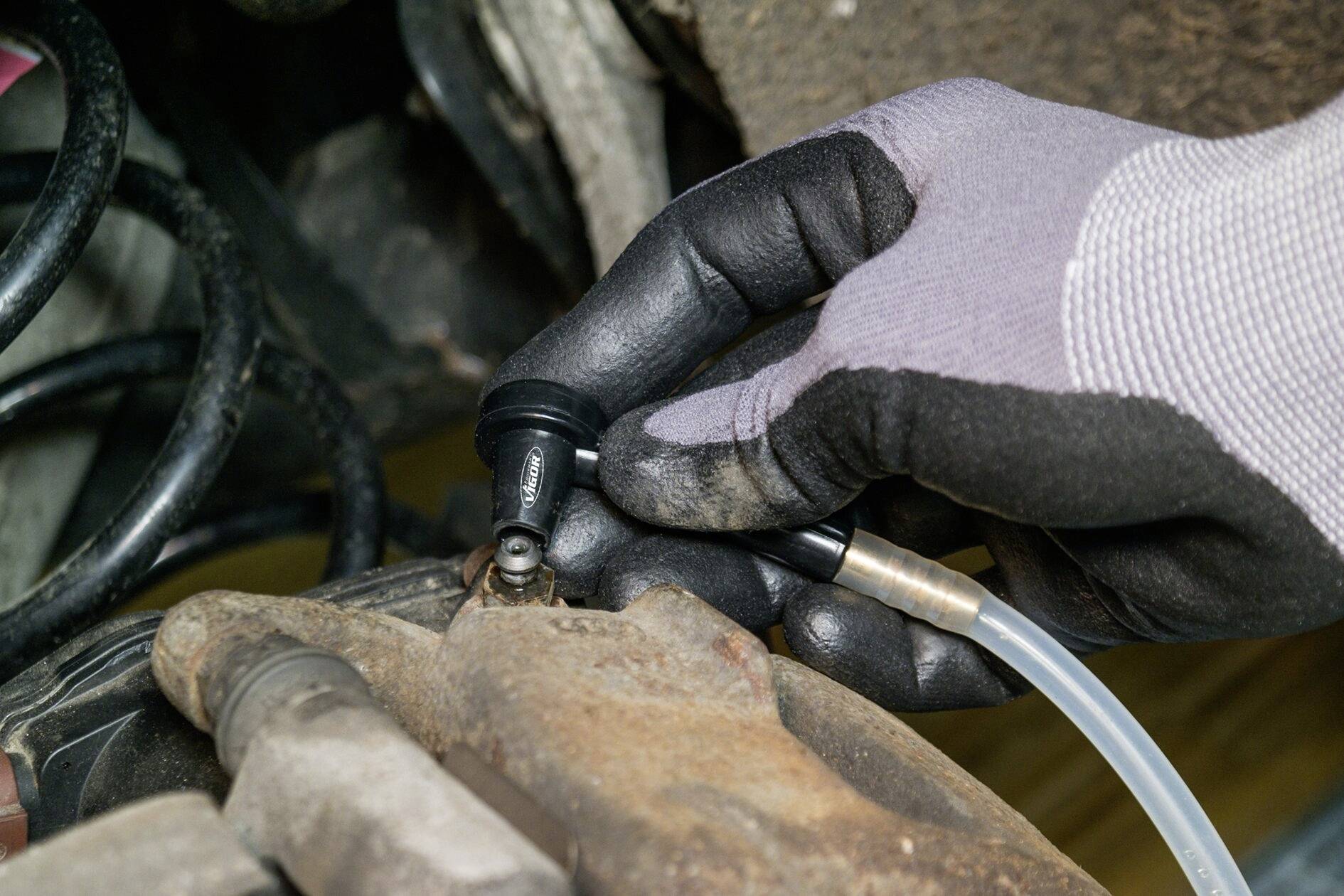 Rukavicí chráněná ruka odvzdušňuje brzdové vedení pomocí speciálního nástroje na brzdovém třmenu automobilu.