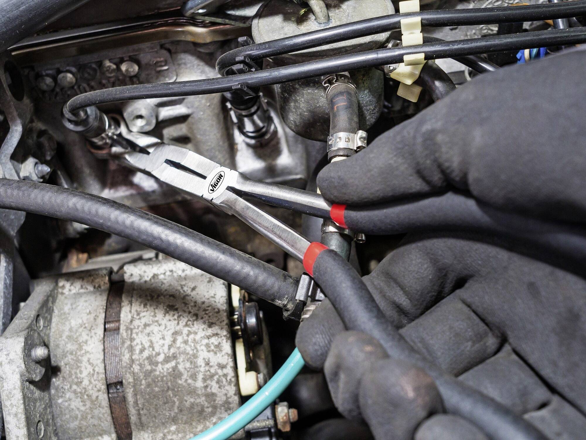 Mechanikovy ruce v rukavicích používají kleště, aby pracovaly na součástce automobilu. Kleště uchopují šroub. Pohled do motorového prostoru.