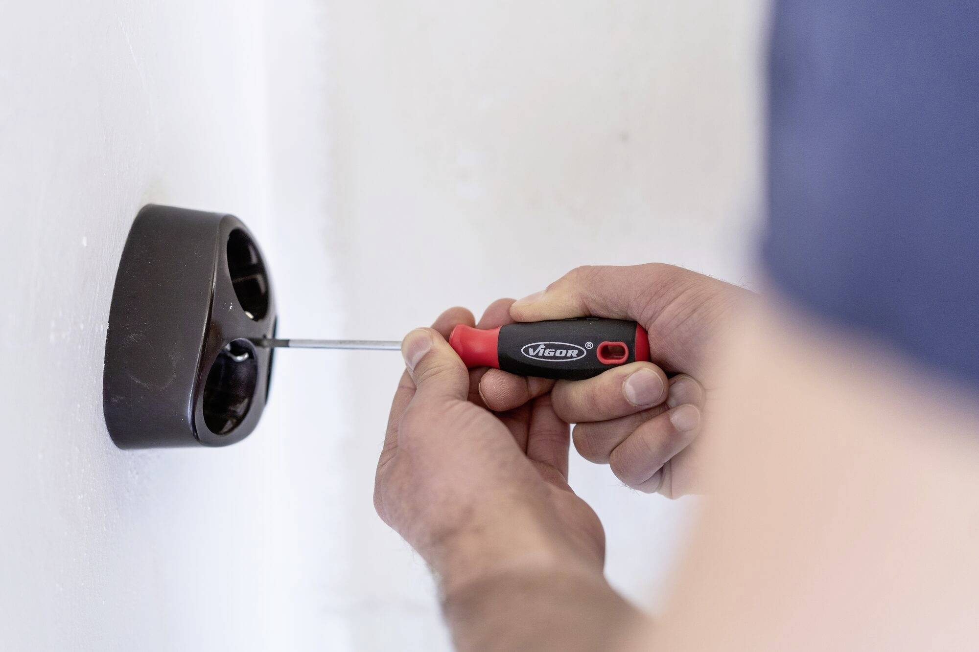 Osoba montuje černý nástěnný držák pomocí šroubováku. V pozadí je vidět bílá stěna.