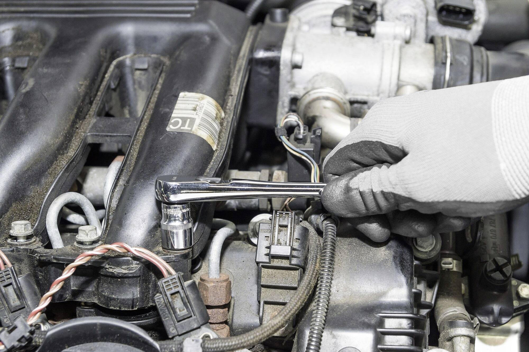 Mechaniká ruka utahuje šroub klíčem na motoru automobilu.