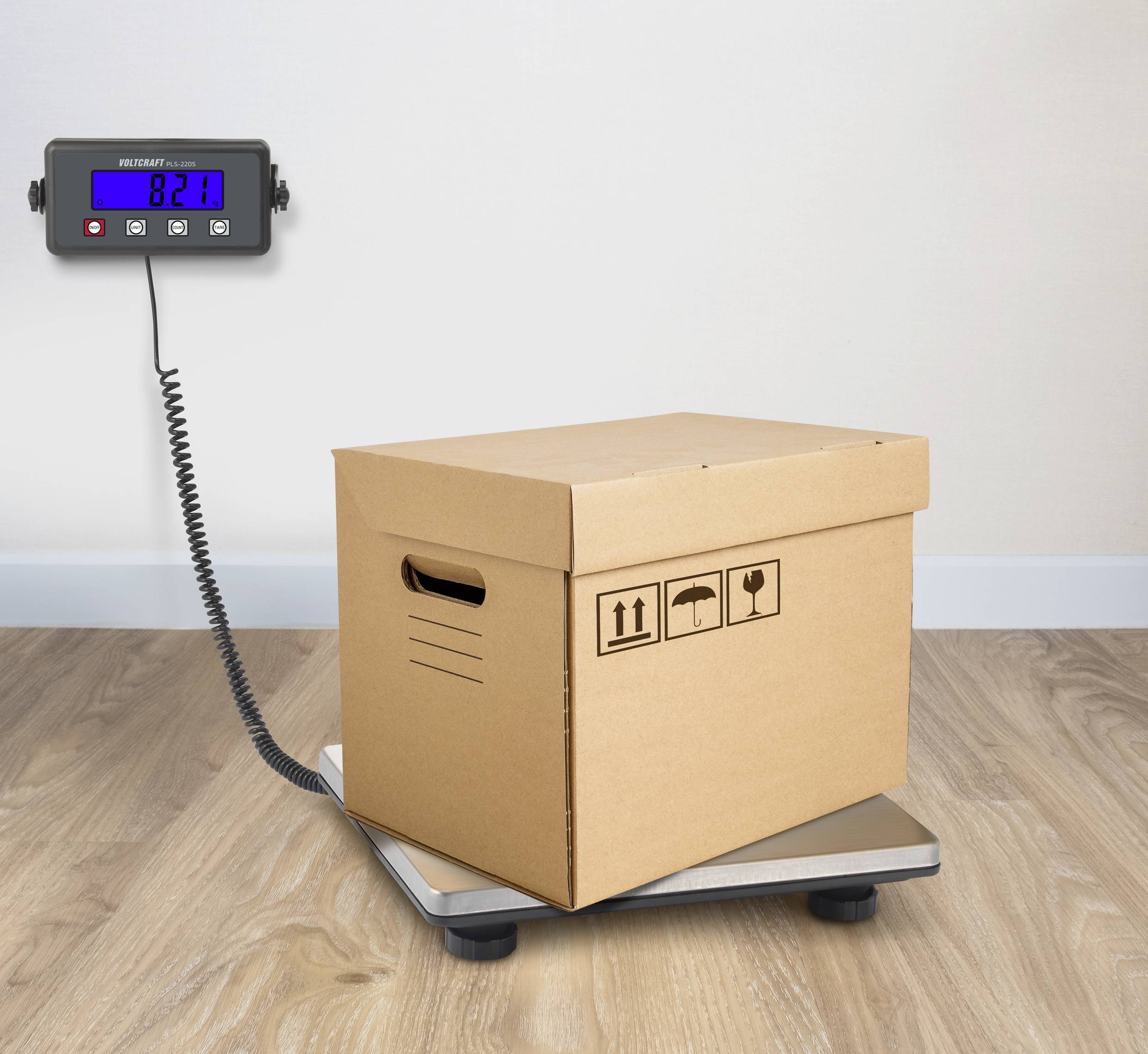 Hnědá krabice je vážena na váze. Digitální displej ukazuje hmotnost 8,21 kg.