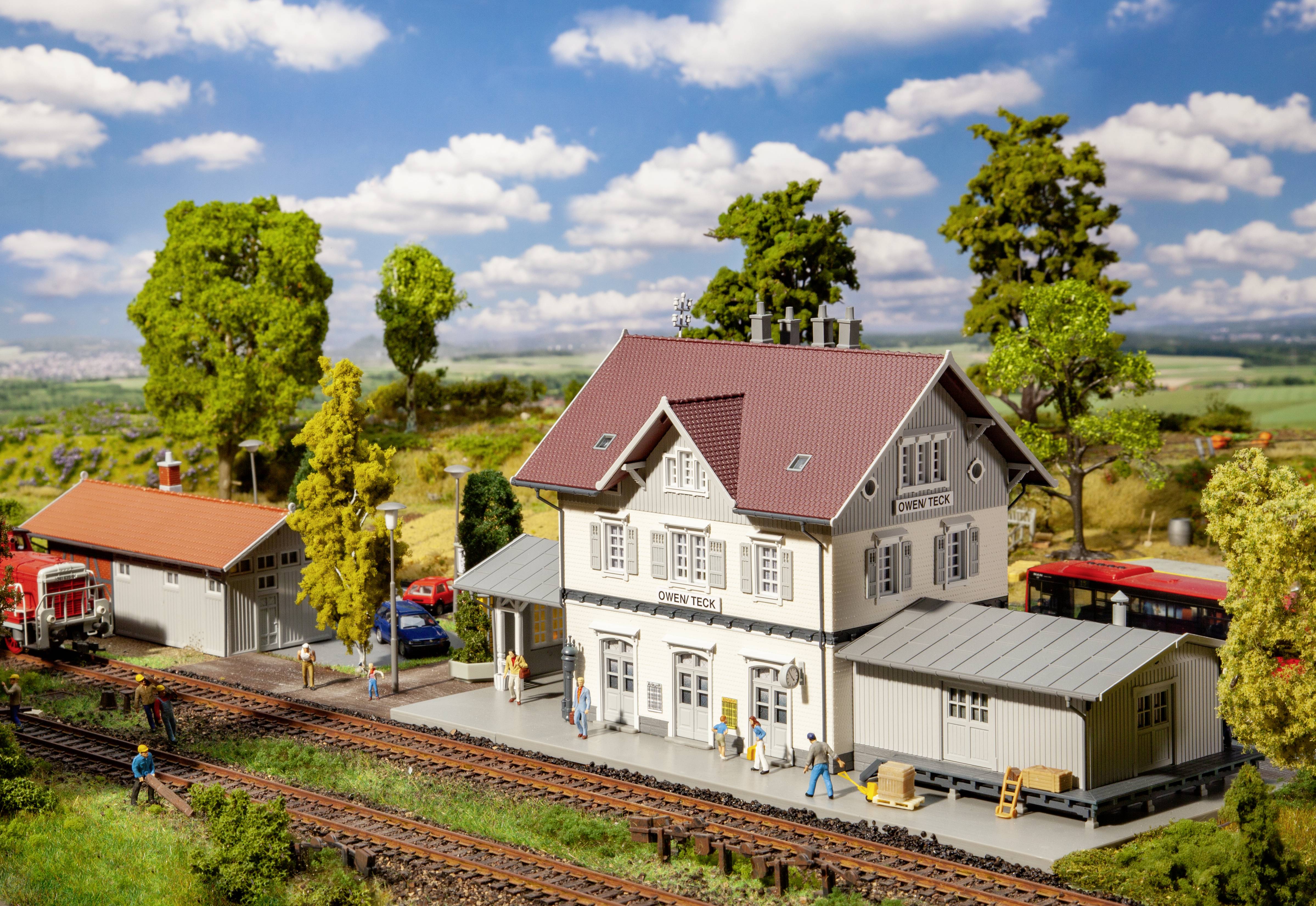 Miniaturní model nádraží s hlavní budovou, vedlejšími budovami a nástupišti. Stromy a louky obklopují tento celek.