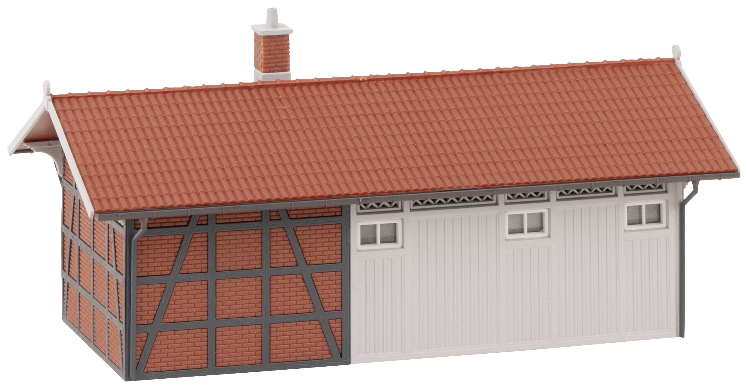 Malá modelová budova ve stylu hrázděné architektury s červenou taškovou střechou, komínem a bílými vraty.
