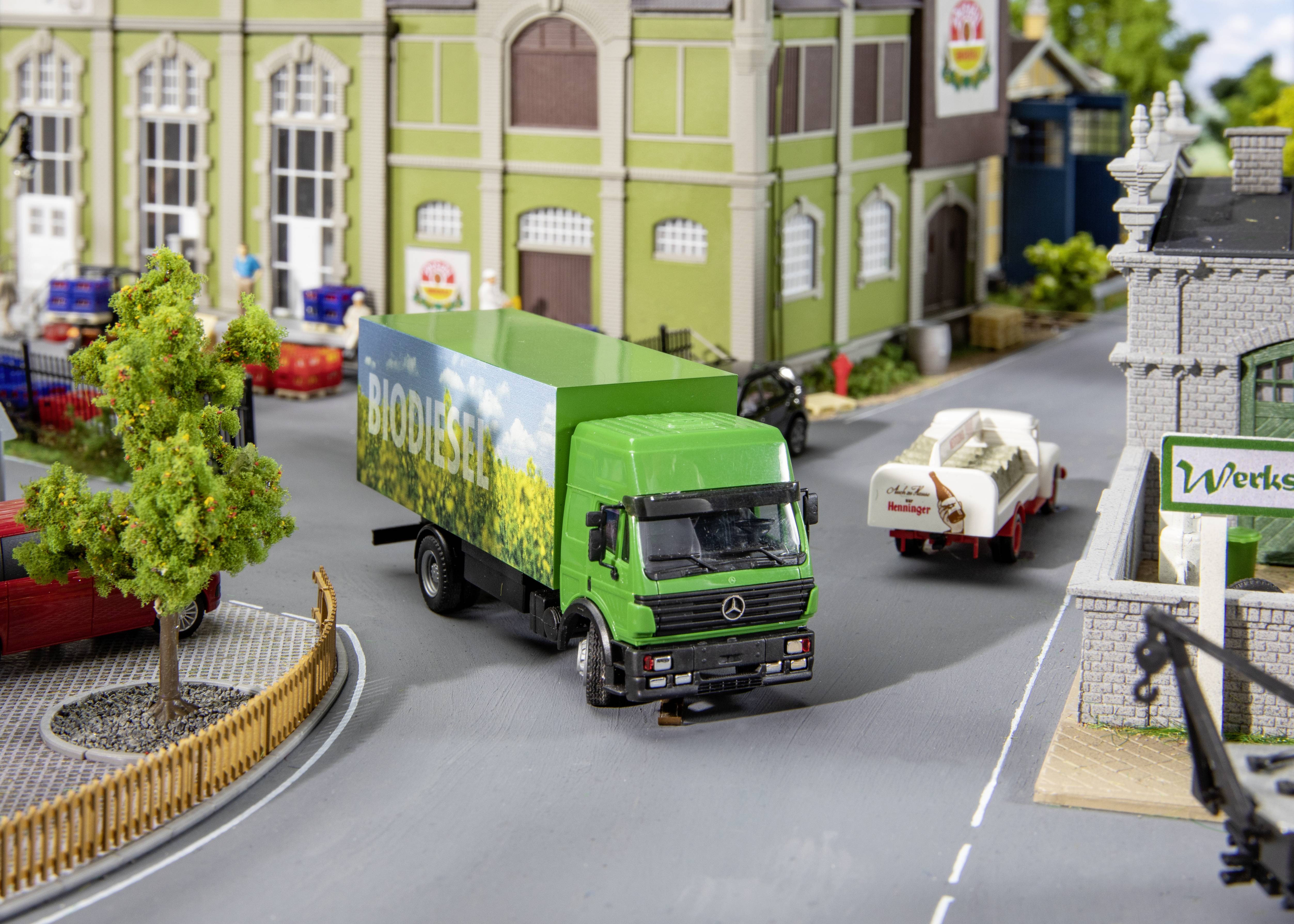 Zelený nákladní vůz s nápisem 'Biodiesel' projíždí miniaturním městem s budovami a zaparkovanými auty.