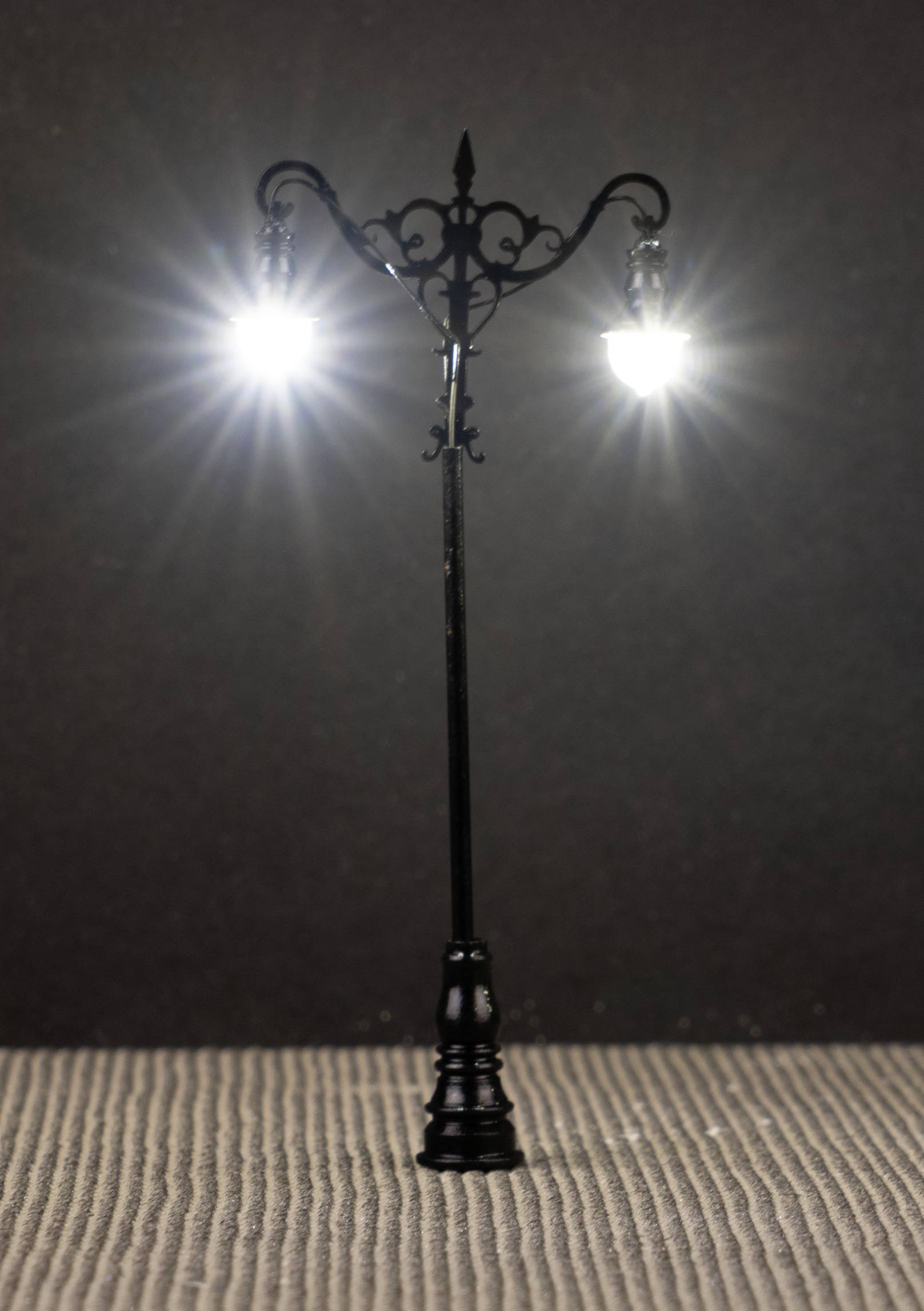 Litinový pouliční lampa se dvěma svítícími žárovkami na tmavém pozadí.