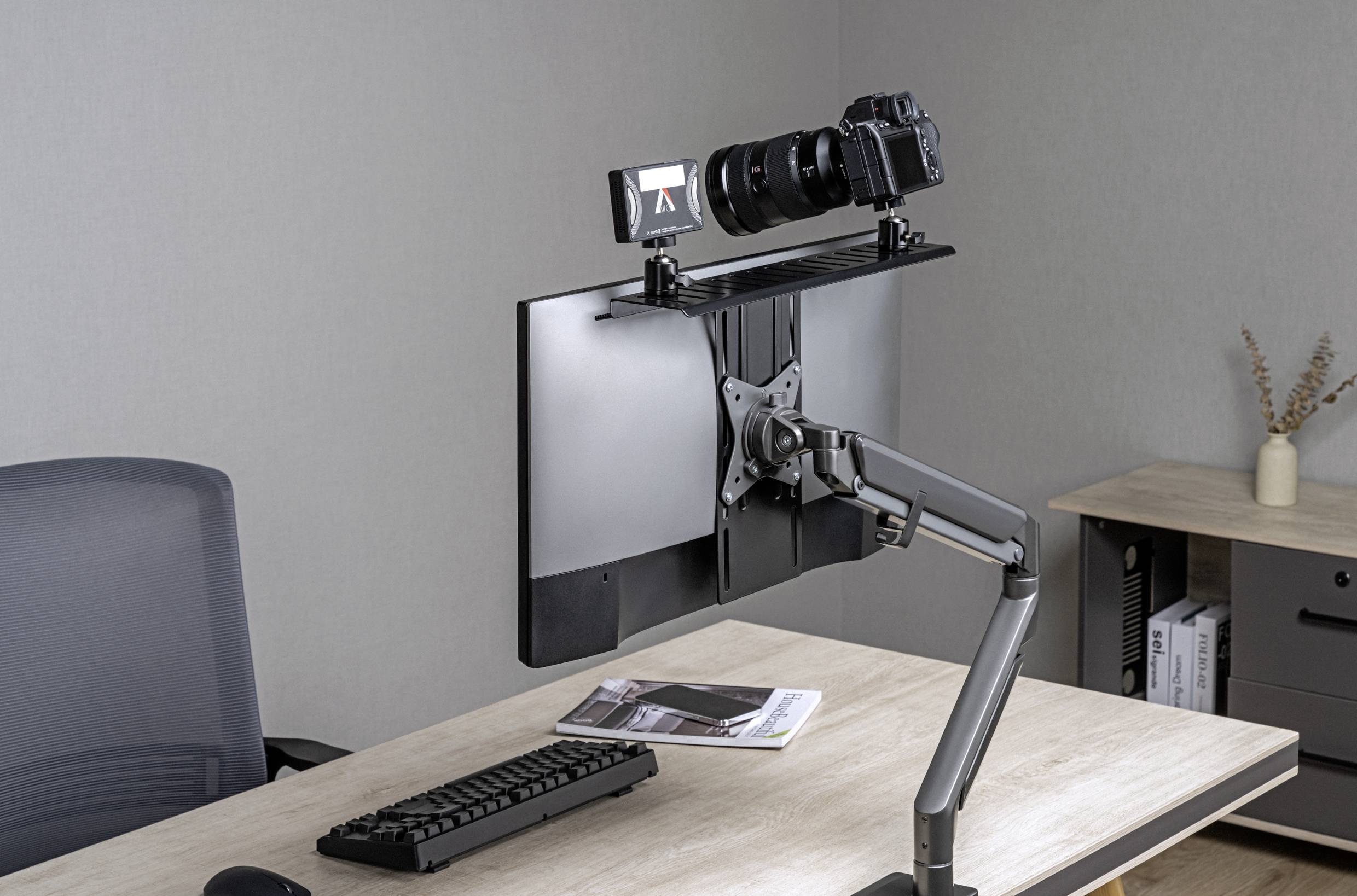 Kamera je upevněna na otočném rameni nad počítačovým monitorem. Pod ním leží klávesnice na dřevěném stole.