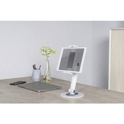 Tablet leží na bílém stojanu na psacím stole. Vedle něj jsou položený notebook a smartphone. V pozadí je váza s rostlinou.