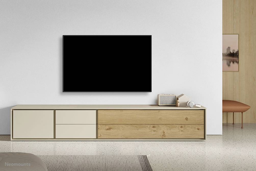 Minimalistický obývací pokoj s velkým televizorem na stěně. Pod ním stojí jednoduché sideboard ozdobené dekorativními předměty.