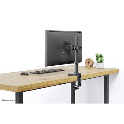Držák monitoru na dřevěném stole s klávesnicí a myší. V pozadí rostlina a hodiny.