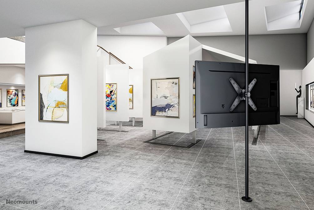 Moderní umělecká galerie s bílými stěnami, abstraktními obrazy a obrazovkou na černém stojanu. Jasné osvětlení.