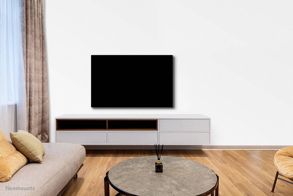 Obývací pokoj s béžovou pohovkou, kulatým konferenčním stolem a nástěnnou plochou televizí nad nízkým TV stolkem. Minimalistické zařízení.