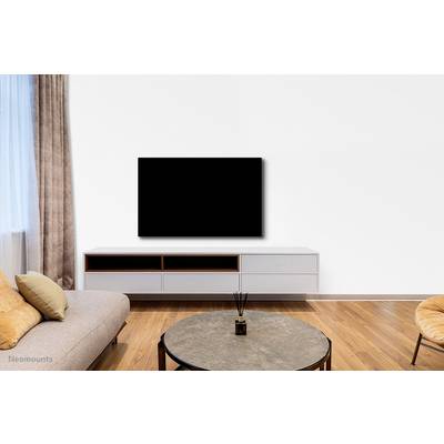 Obývací pokoj s béžovou pohovkou, kulatým konferenčním stolem a nástěnnou plochou televizí nad nízkým TV stolkem. Minimalistické zařízení.