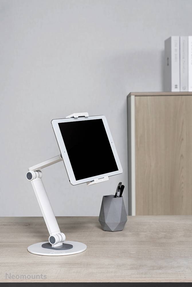 Počítačový stůl s držákem na tablet, na němž leží tablet. V pozadí skříň s pořadači a stojan na tužky.