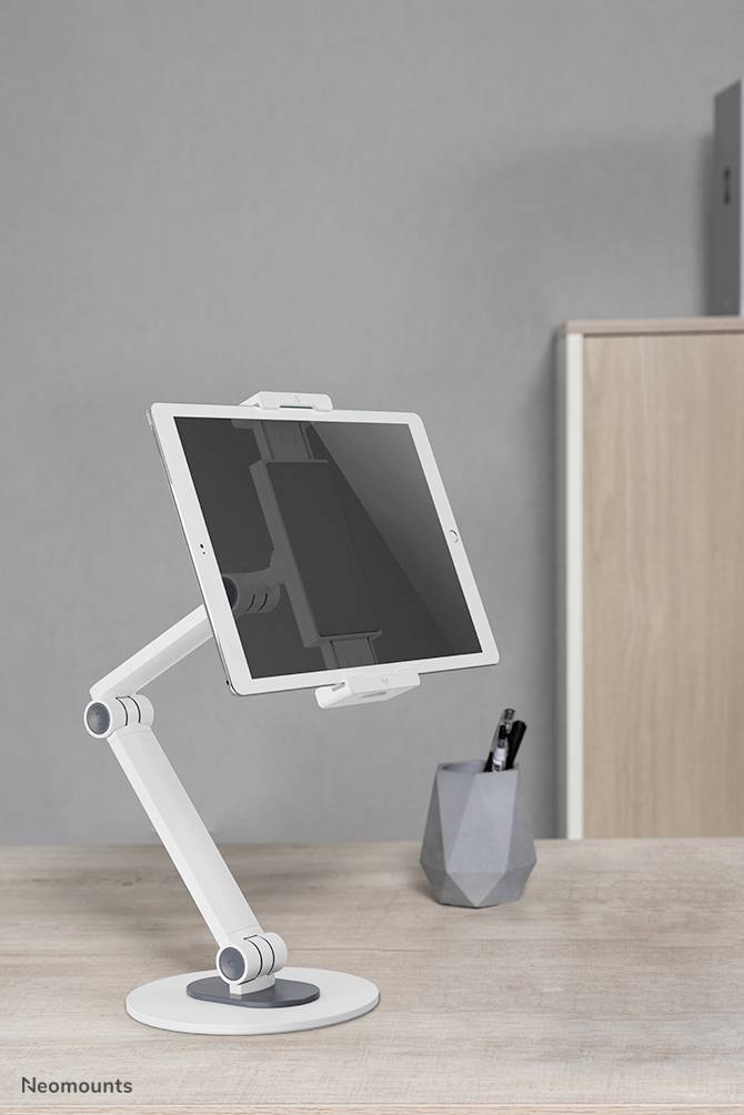 Tablet leží na bílém, nastavitelném držáku na paži, který je umístěn na psacím stole. Vedle něj je stojánek na tužky naplněný psacími potřebami.