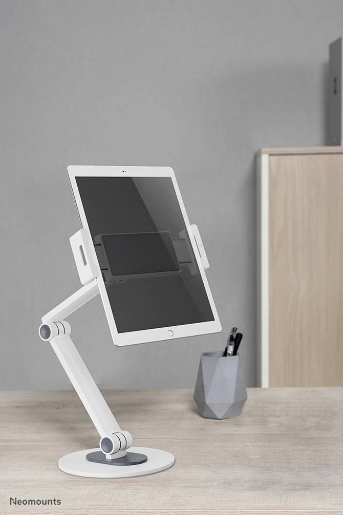 Bílý stojan na tablet drží tablet vzpřímeně na psacím stole. V pozadí stojí nádoba s psacími potřebami.