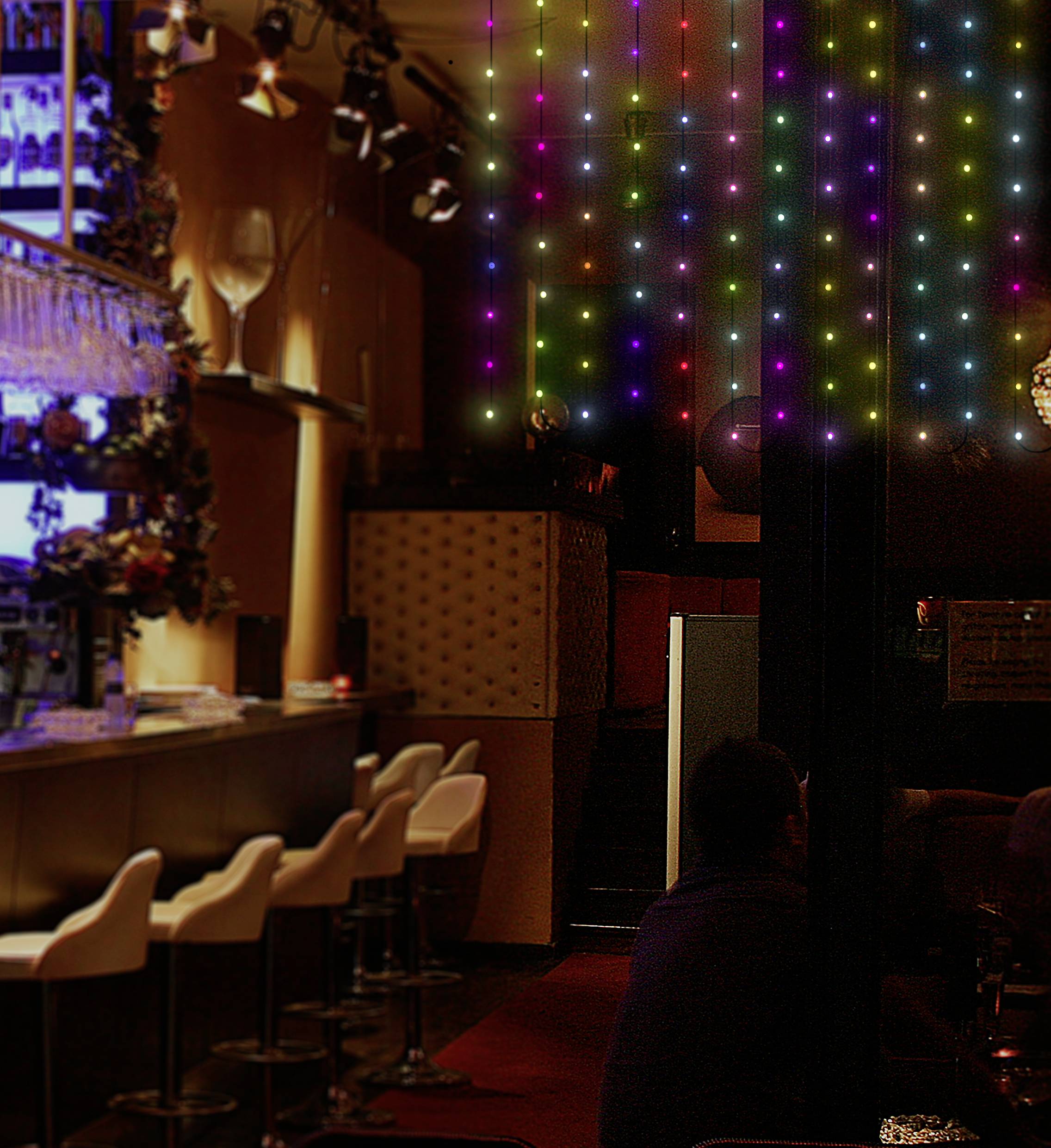 Elegantní bar s prázdnými bílými barovými stoličkami. Vpravo na stěně svítí barevná LED světla. Atmosférické osvětlení.