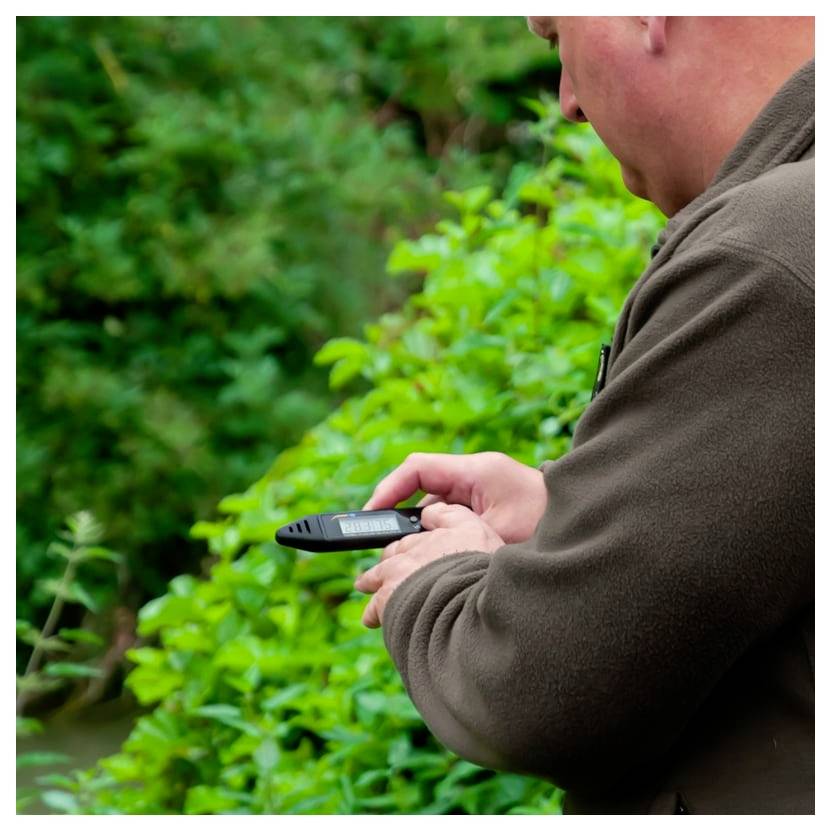 Muž venku poblíž husté zeleně, drží a používá přenosné zařízení GPS nebo telefon, zatímco se na něj dívá.