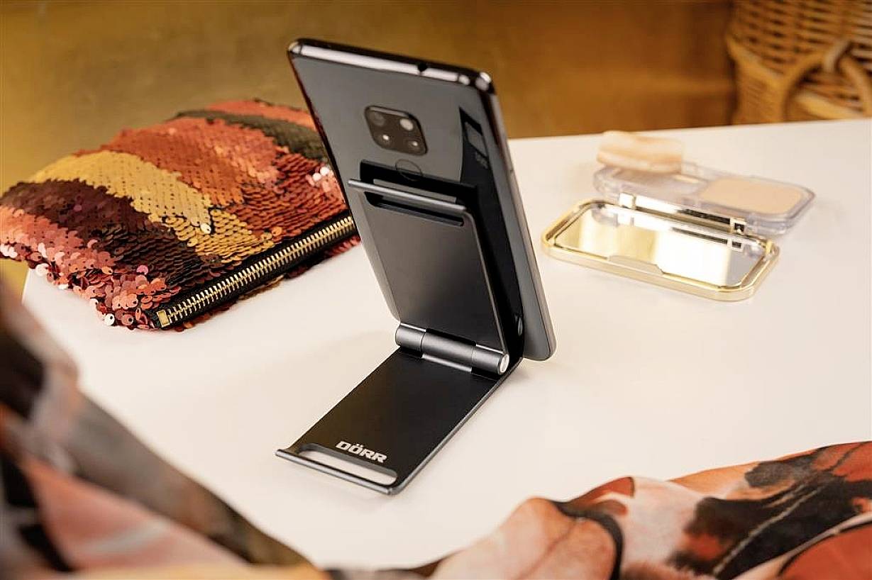 Smartphone na nastavitelném stojánku na stole, obklopené třpytivou kabelkou a otevřenou sadou make-upu.