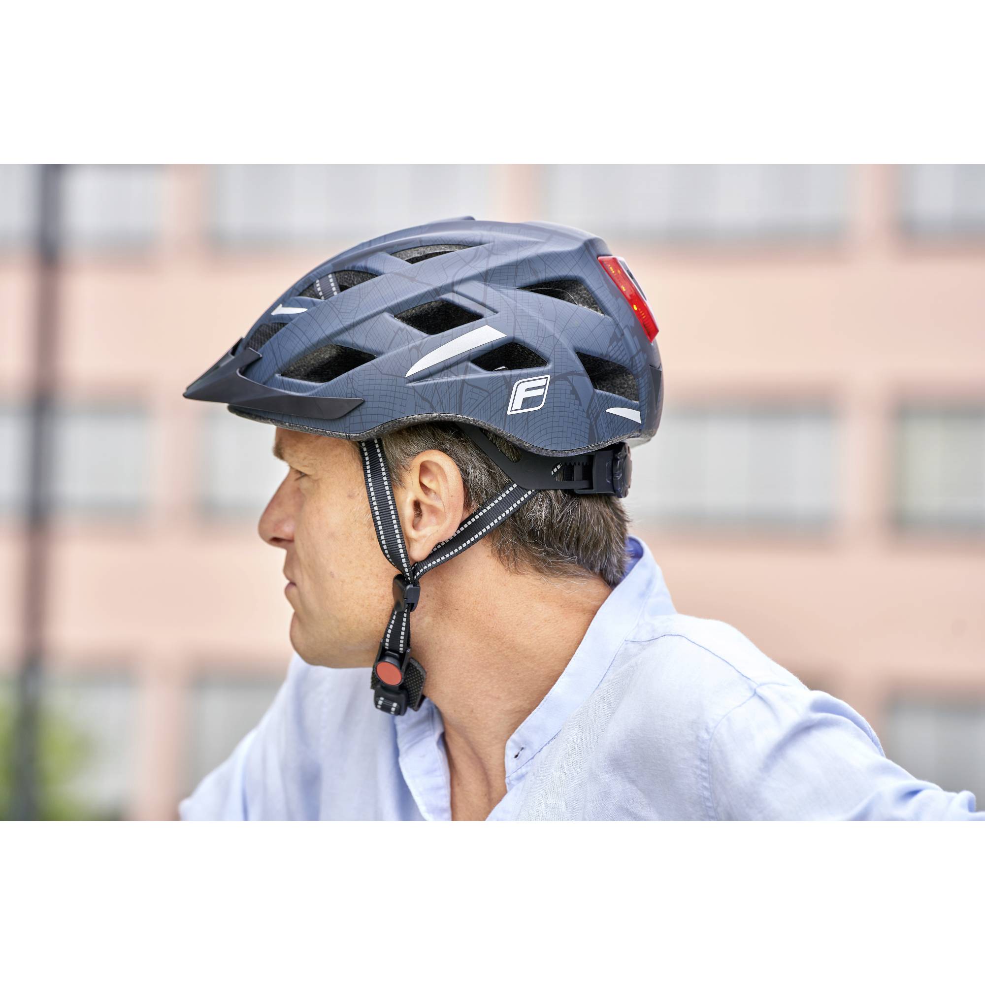 Člověk s modrým cyklistickou helmou se dívá stranou. V pozadí je rozmazaná budova.