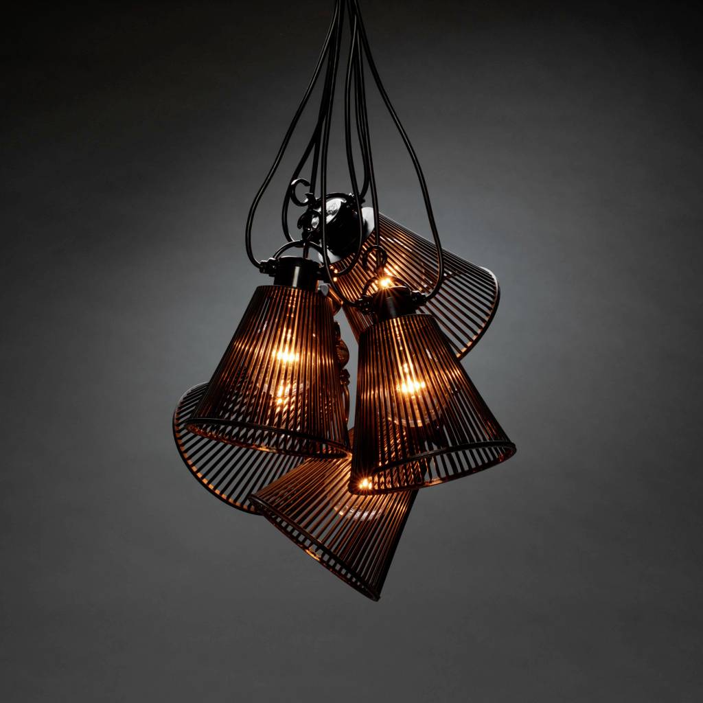 Moderní závěsná lampa s pěti světélkujícími stínidly z drátů, spojenými v jednom bodě, visí v tmavé místnosti.