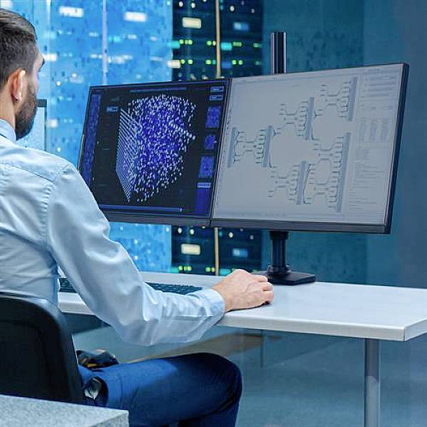 Osoba pracuje na počítači se dvěma monitory a analyzuje data před pozadím serverů.