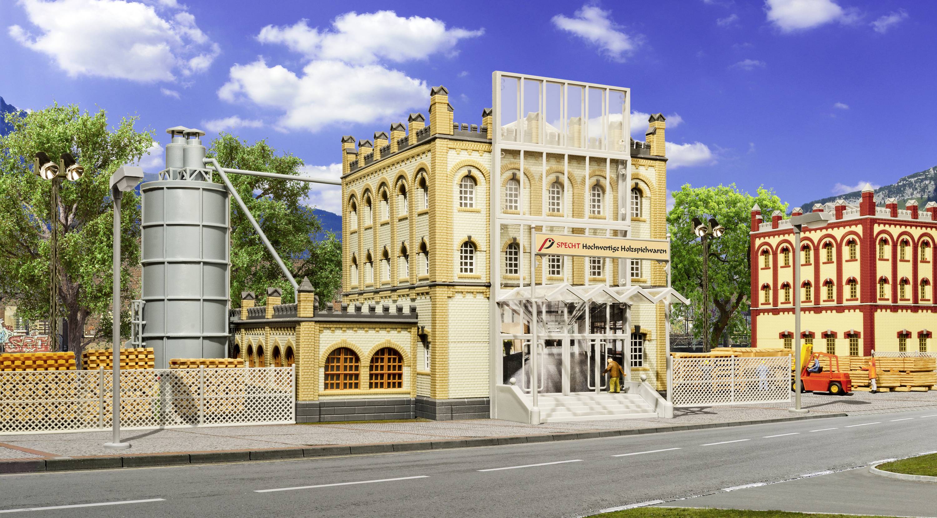 Model historické tovární budovy se žlutými fasádami a obloukovými vraty. Vedle stojí stříbrná sila.
